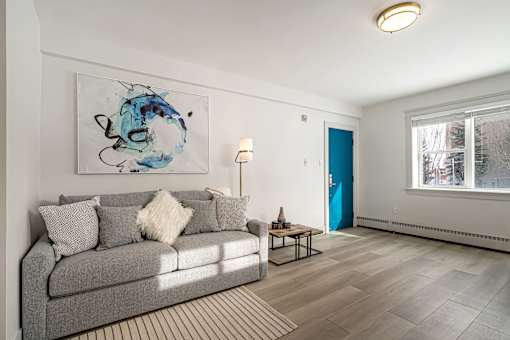 A living room with a grey couch and a blue abstract painting on the wall.
