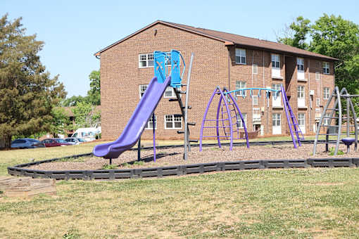 A purple slide in a playground in front of a brick building.