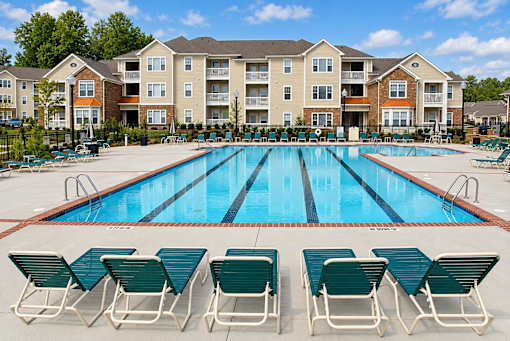 A swimming pool surrounded by lawn chairs in front of apartment buildings.