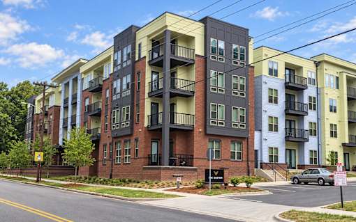 A row of apartment buildings with balconies and a car parked in front.