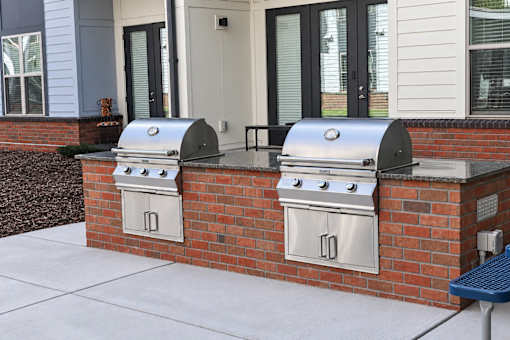 Two silver barbecues are built into a brick wall.