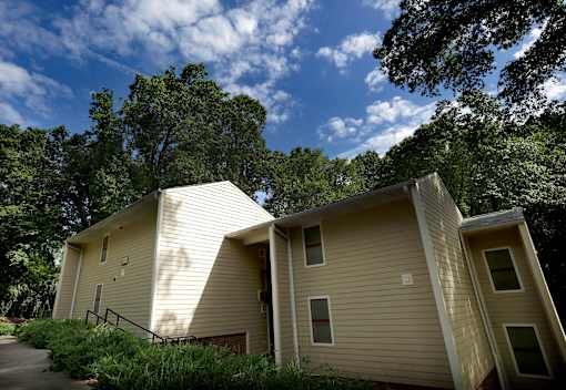 A beige house with a sloped roof is surrounded by trees.