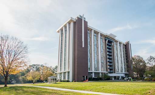 A large, modern building with a red and white facade stands in a grassy area with trees in the background.