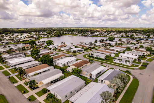 A large white building with a grey roof is surrounded by other buildings and trees.