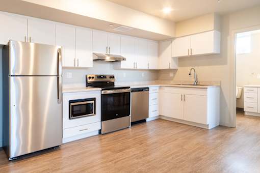 A modern kitchen with a stainless steel refrigerator and white cabinets. at All Saints Apartments, Colorado