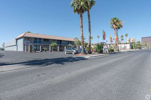 A street view with an apartment building, palm trees, and a car.