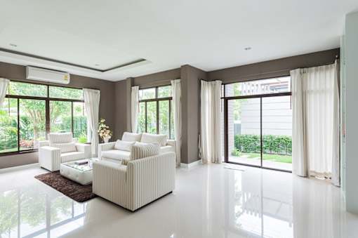 A spacious living room with a white sofa set and large windows.