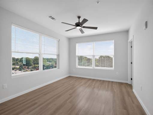 A room with a ceiling fan and two windows.