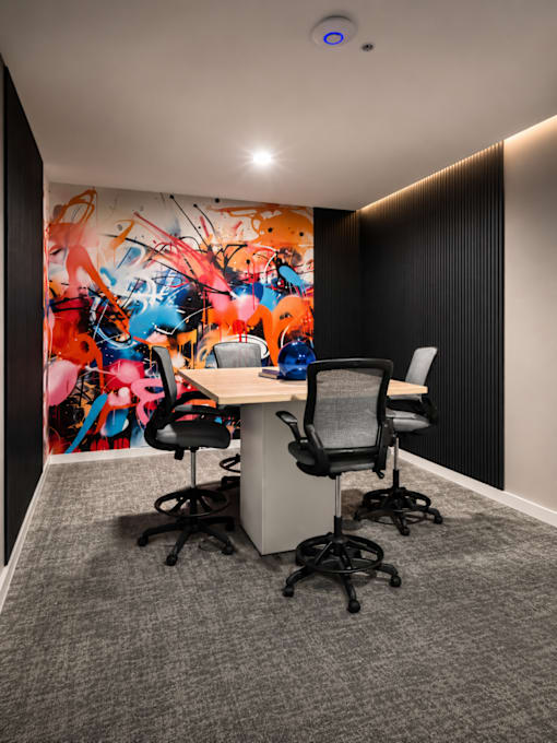 Modern private podcast room with a collaborative meeting table, ergonomic seating, colorful mural wall, and acoustic paneling at 200 Main Kannapolis.
