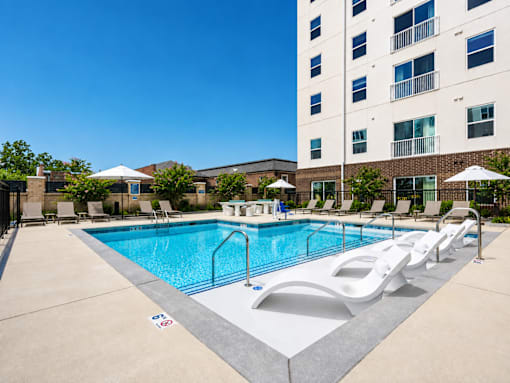 A large swimming pool with lounge chairs and umbrellas in front of a tall building.
