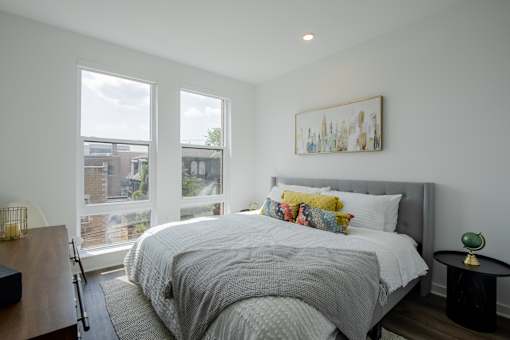 Modern bedroom at The Rail Bound Brook with three large windows, city views, and a cozy bed—offering comfort and elegance in NJ apartment living.