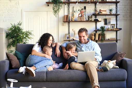 A family of four is sitting on a couch with a laptop.