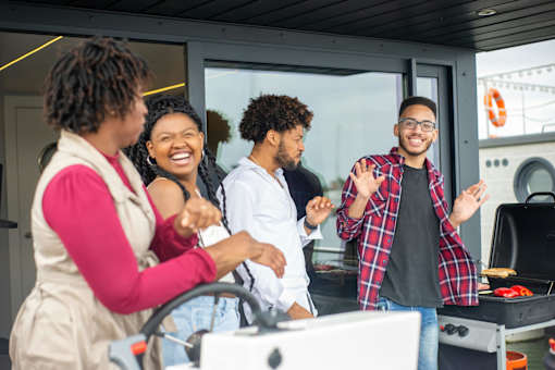 Four people are standing in front of a grill, smiling and laughing together.