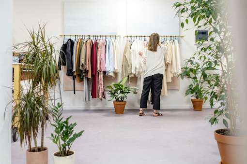 A woman is looking at clothes on a rack in a room with potted plants.