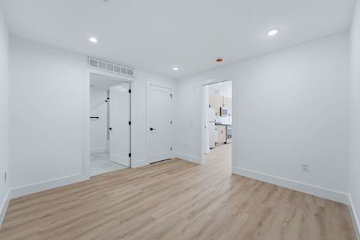 A white room with wood flooring and a doorway leading to another room.