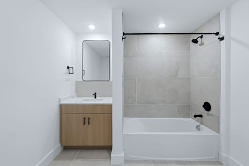 A white bathroom with a sink, mirror, and bathtub.