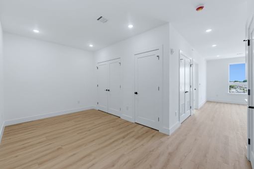 A room with white walls and wooden flooring, featuring a row of white cupboards.