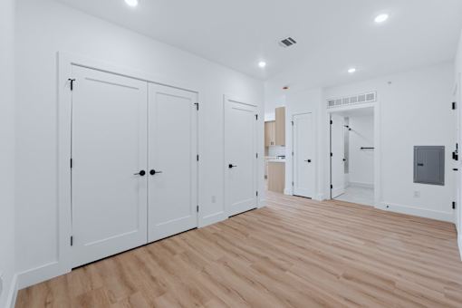 A room with white walls and wooden flooring, featuring a row of white doors with black handles.