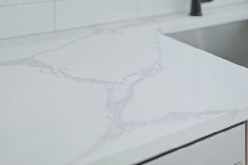 A close up of a white marble countertop with a sink in the background.