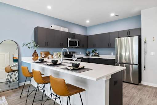 A modern kitchen with a white island and brown chairs.
