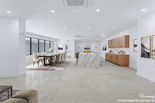 A spacious, well-lit party room with a dining table and chairs, a kitchen area, and a large window.