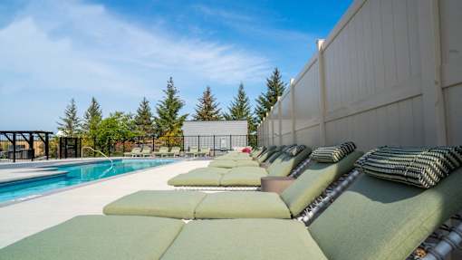 A row of green cushioned lounge chairs are arranged on a patio next to a pool.