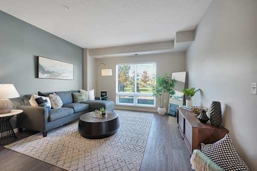 A living room with a grey couch, a coffee table, and a large window.