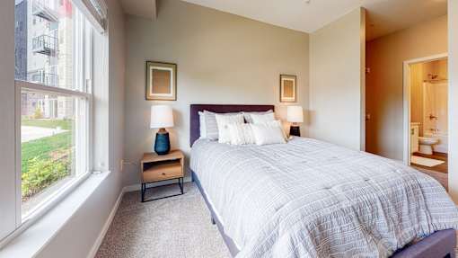 A bedroom with a large bed and a window overlooking a green lawn.