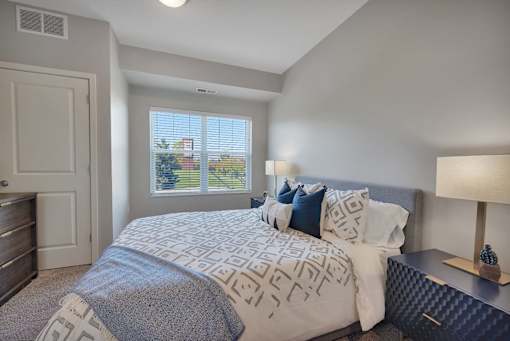 A bedroom with a large bed and a window with blinds.