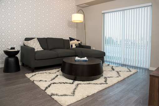 A grey couch with a white pillow is in front of a wallpapered wall.