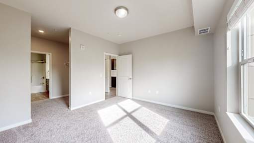 A spacious room with a carpeted floor and a window on the right side.