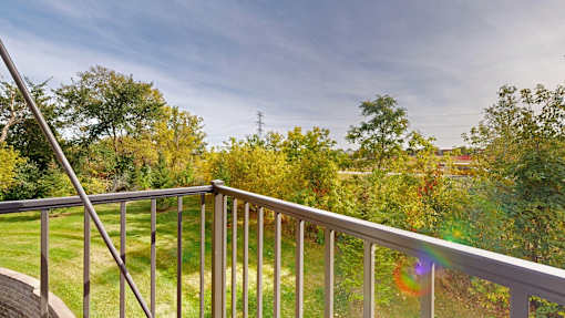 A balcony with a metal railing overlooks a green lawn and trees.