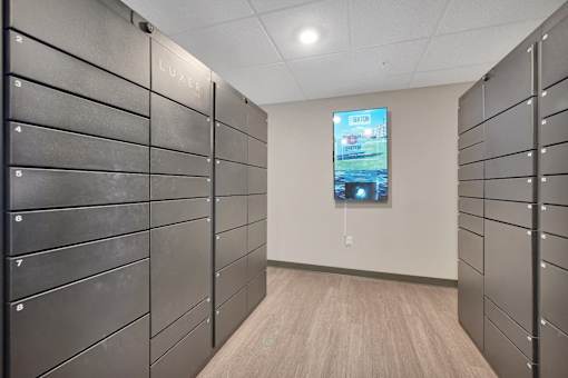 A hallway with a row of lockers on the left and a TV screen on the right.