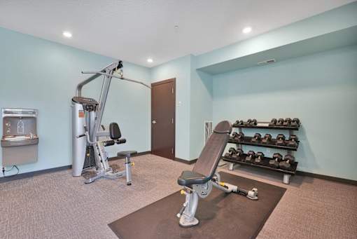 A gym room with a variety of equipment including a treadmill, weights, and a bench press.
