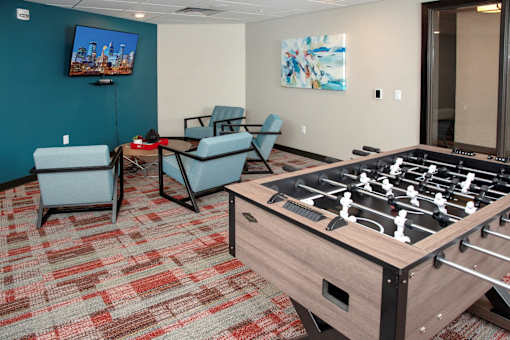 A foosball table is in the middle of a room with two chairs and a television.