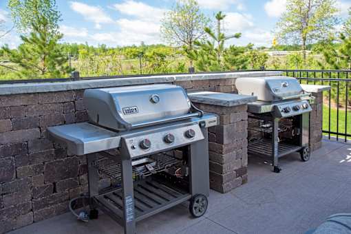 Two grills on a patio with a brick wall.