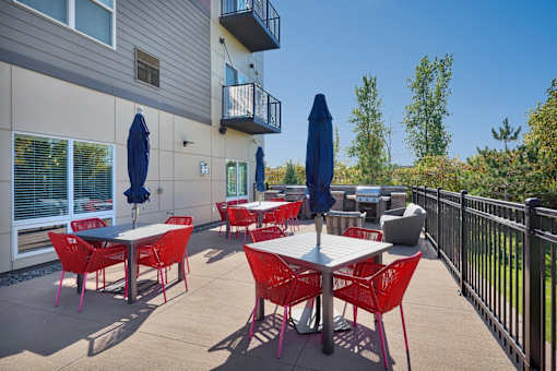 A patio with red chairs and tables is surrounded by a black fence.