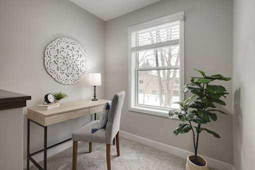 A room with a desk, chair, and a plant.
