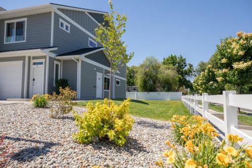 a blue house with a white fence and a yard with yellow flowers at The Brix Apartments, Spokane Valley, WA, 99037