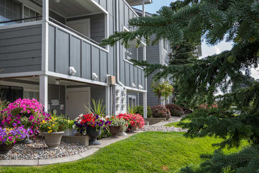 A grey building with a balcony and a garden in front of Morning Glory Circle Apartments, 99208