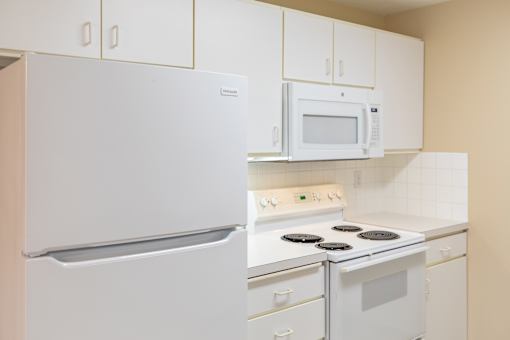 A white refrigerator and microwave are in a kitchen with white cabinets.