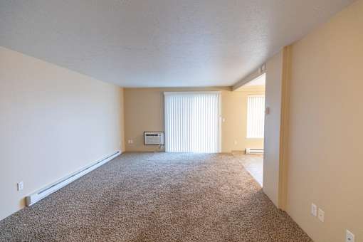 A spacious room with a carpeted floor and a window with blinds.