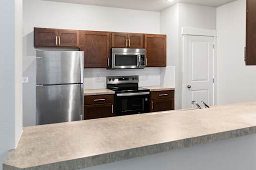A kitchen with a stainless steel refrigerator, microwave, oven, and wooden cabinets.at The Brix Apartments, Spokane Valley, 99037