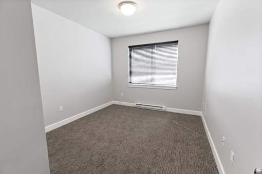 A room with a carpeted floor and a window with blinds.at The Brix Apartments, Spokane Valley, WA