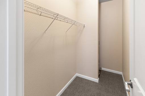 A white door is open to a hallway with a carpeted floor and a metal rack on the wall.