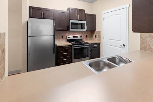 A kitchen with a refrigerator, microwave, oven, and sink.
