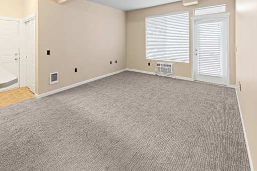 A room with a carpeted floor and a window with blinds.