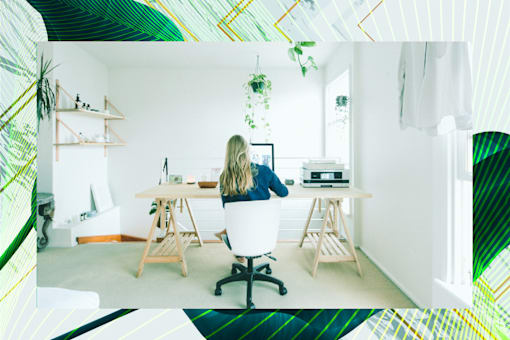 A woman is sitting at a desk in a room with a laptop and a plant.
