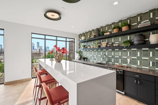 Community rooom kitchen with a white counter top and a large island with red chairs
