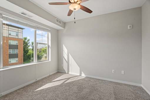 A room with a ceiling fan and a window overlooking a building.